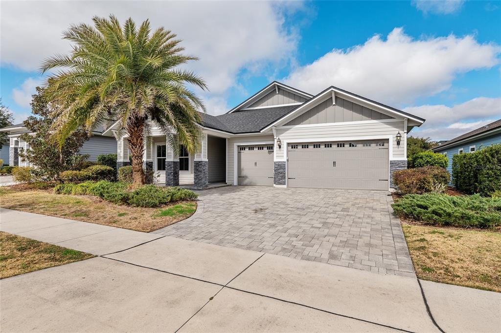 A single-story house with a gray garage, stone accents, and a palm tree in front — 11890 SW 33RD LANE, GAINESVILLE, FL