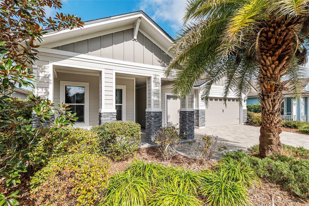 A single-story house with beige siding, stone accents, a covered porch, and a palm tree — 11890 SW 33RD LANE, GAINESVILLE, FL