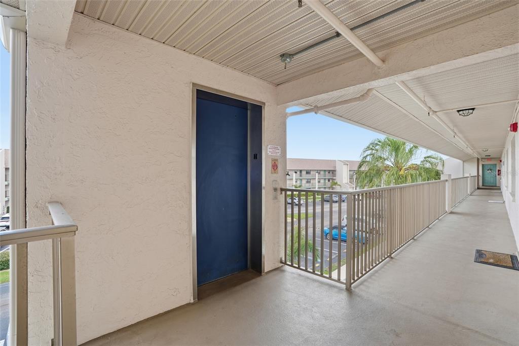 An outdoor walkway features a blue elevator door, a metal railing, and a concrete floor — 175 KINGS HIGHWAY UNIT 635, PUNTA GORDA, FL