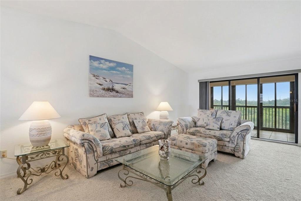 A living room with patterned sofas, a glass coffee table, and a balcony with outdoor views — 175 KINGS HIGHWAY UNIT 635, PUNTA GORDA, FL