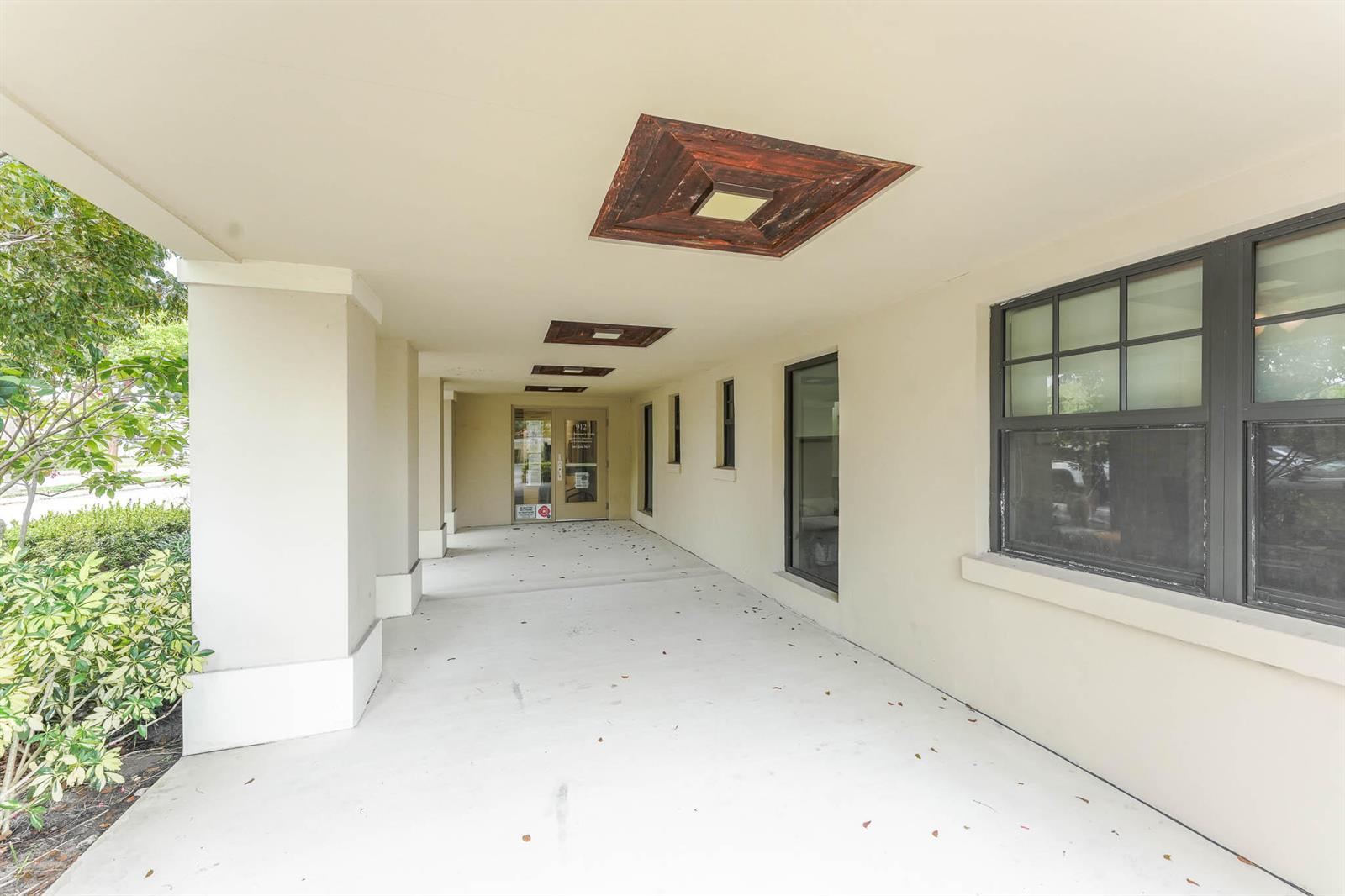 A covered exterior walkway features a concrete floor, recessed wooden ceiling panels, and glass doors — 912 SE 4th Street, Boynton Beach FL 33435, BOYNTON BEACH, FL