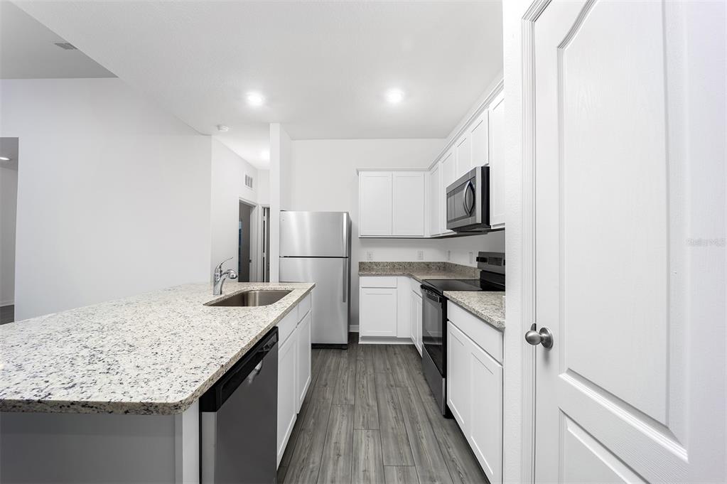 A kitchen features white cabinets, granite countertops, stainless steel appliances, and gray wood-look flooring — 1342 CONGO COURT, POINCIANA, FL
