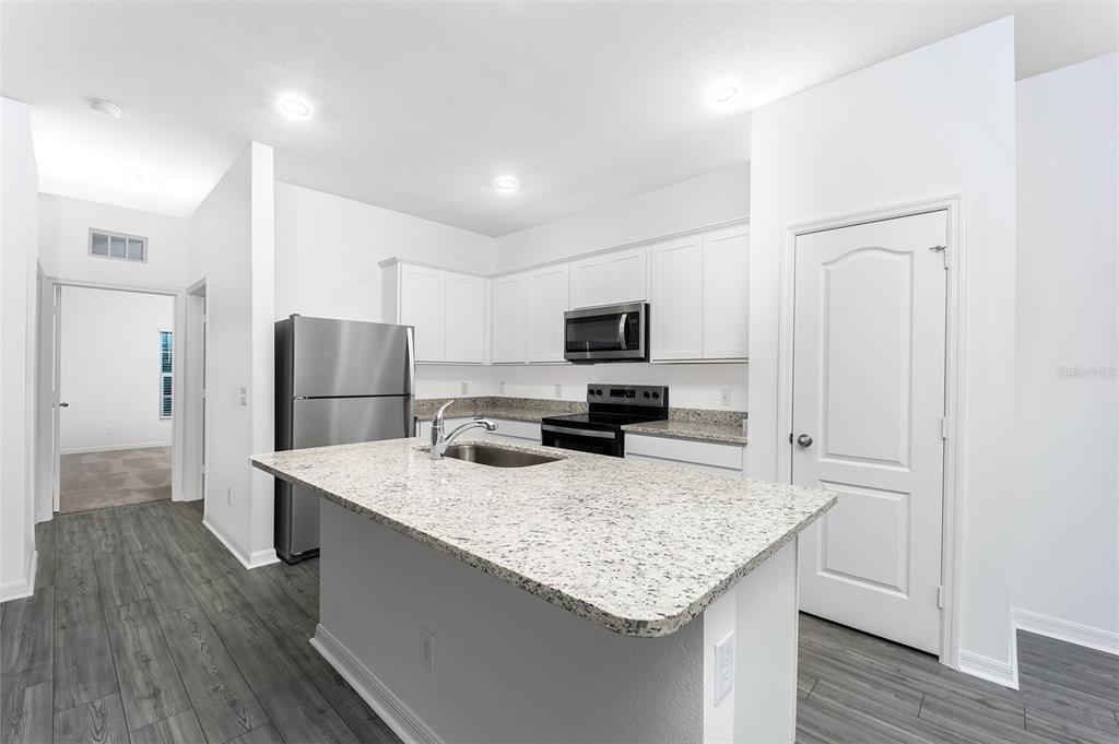 A kitchen with white cabinets, stainless steel appliances, a granite island, and gray wood flooring — 1342 CONGO COURT, POINCIANA, FL