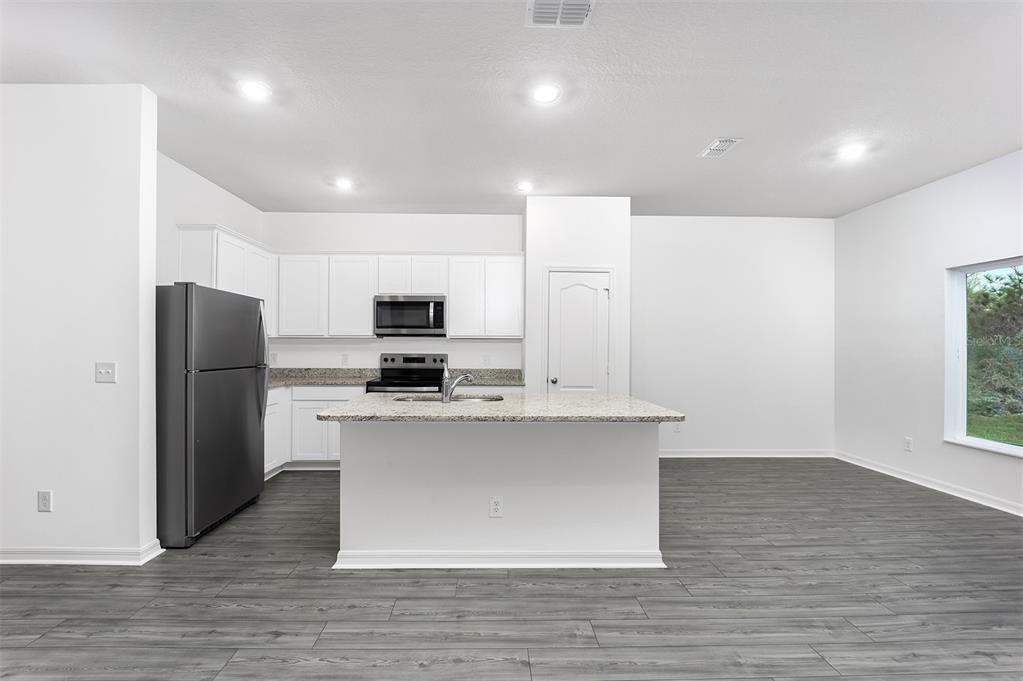 A kitchen with white cabinets, granite countertops, stainless steel appliances, and gray wood-look flooring — 1342 CONGO COURT, POINCIANA, FL
