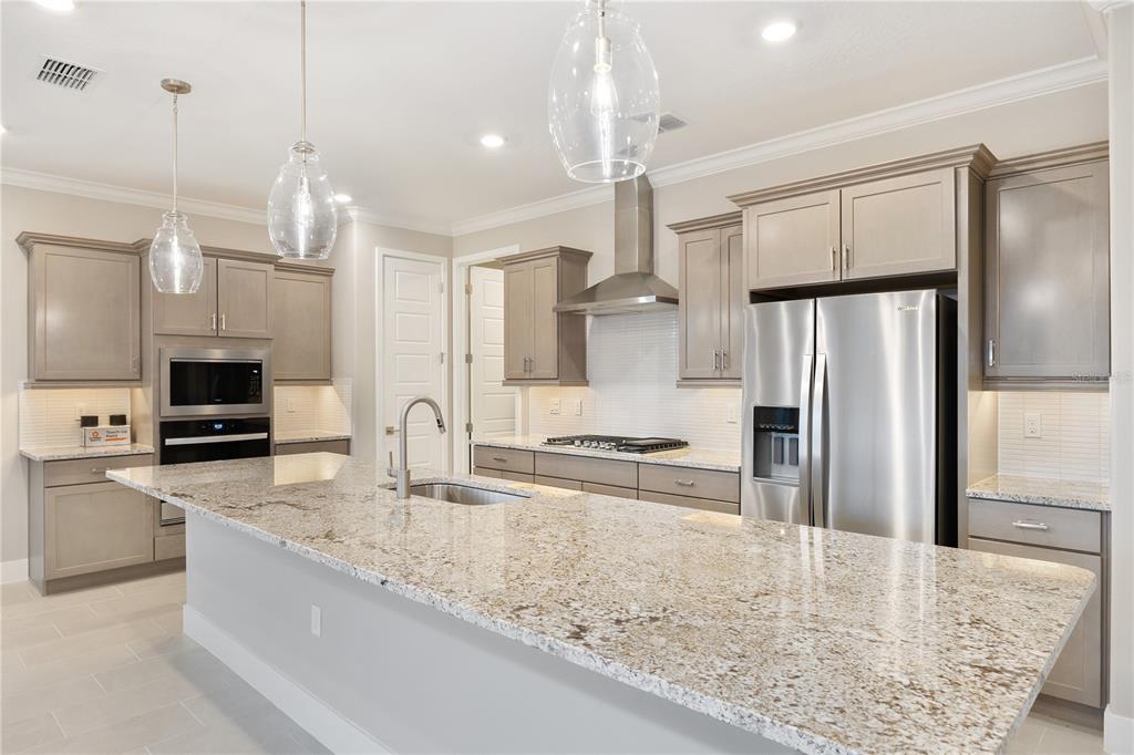 A modern kitchen features gray cabinets, granite countertops, stainless steel appliances, and a large island — 4457 NW 53RD AVENUE, OCALA, FL