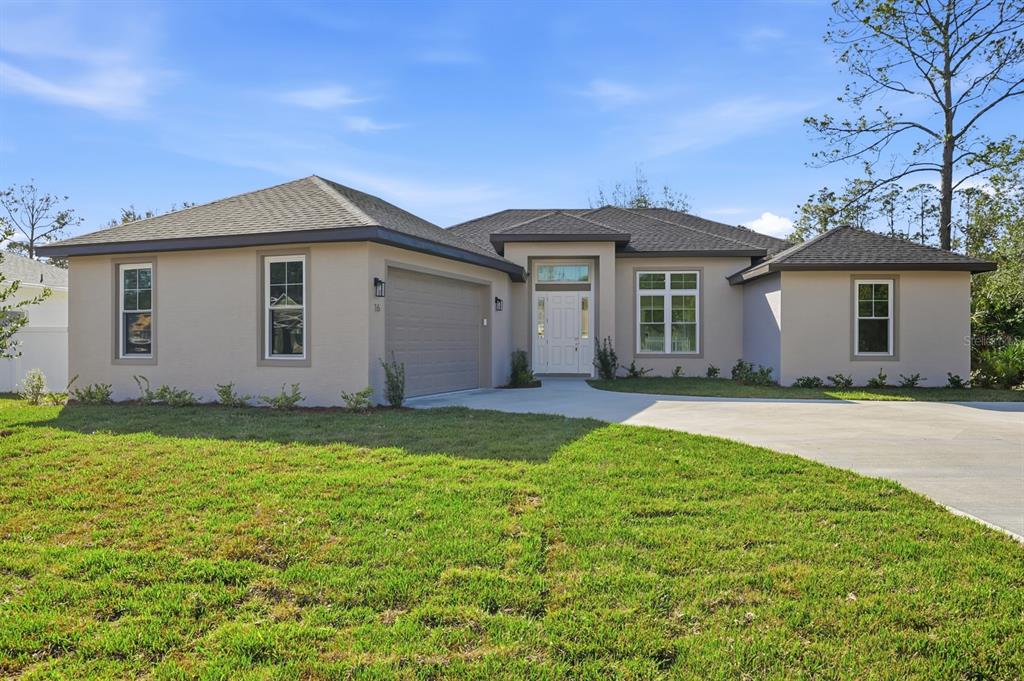 A single-story house with a beige stucco exterior, a two-car garage, and a concrete driveway — 16 PIERCE LANE, PALM COAST, FL
