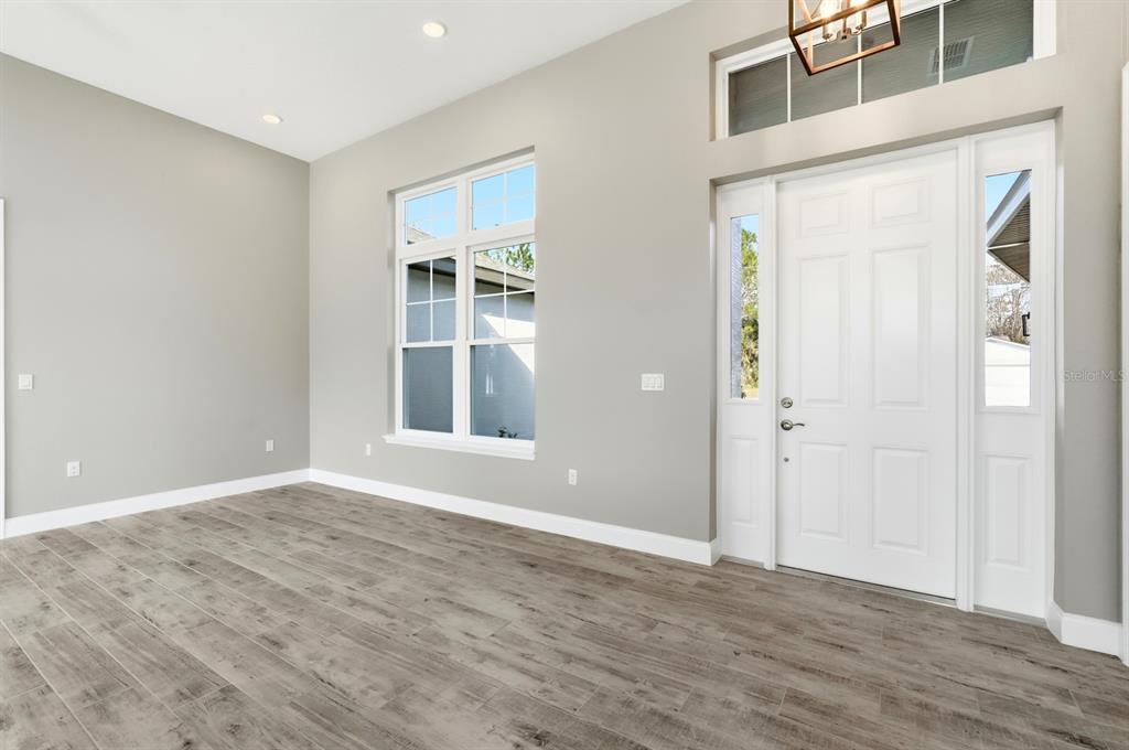 An empty room features light gray walls, wood-look tile flooring, a white front door, and windows — 16 PIERCE LANE, PALM COAST, FL