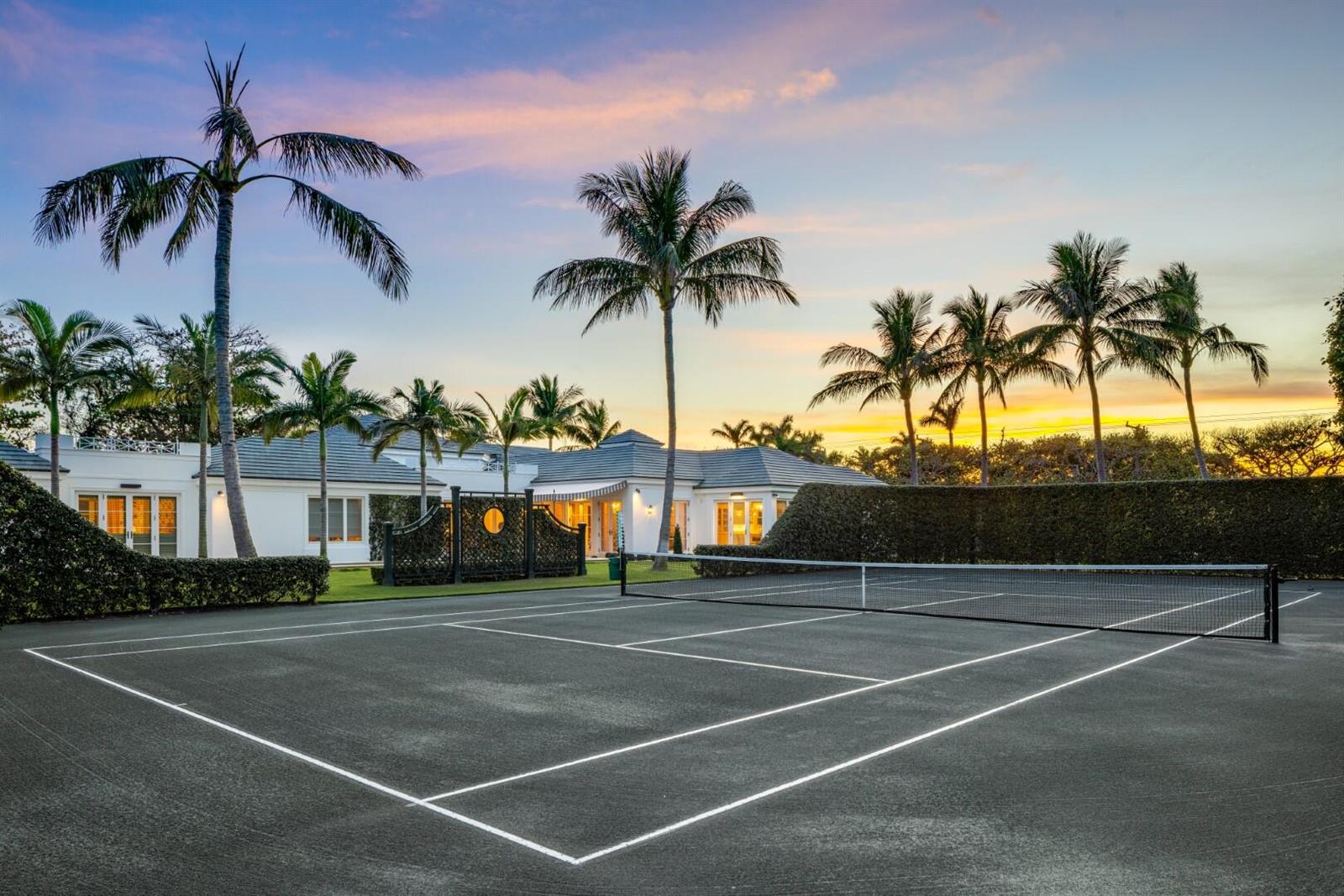 A tennis court sits in front of a white house surrounded by palm trees at sunset — 710 S County Road, Palm Beach FL 33480, PALM BEACH, FL