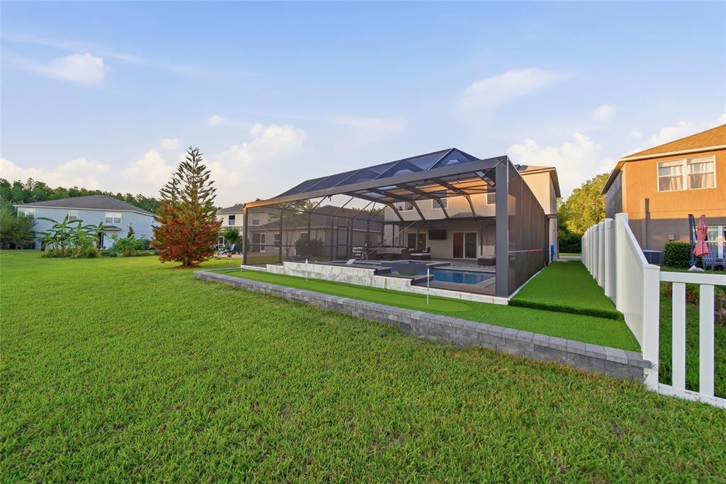 A backyard features a screened-in pool, a putting green, and a stone retaining wall — 18133 BAHAMA BAY DRIVE, TAMPA, FL