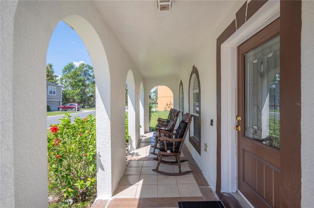 A covered porch features arched openings, tiled flooring, and several wooden rocking chairs — 5155 SPANISH OAKS DRIVE, LAKELAND, FL