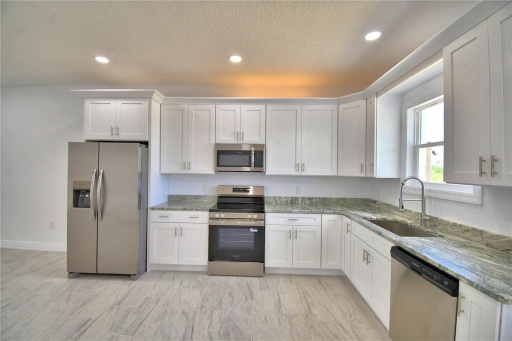 A kitchen features white cabinets, stainless steel appliances, and light-colored granite countertops — 7951 SARASOTA DRIVE UNIT A, INDIAN LAKE ESTATES, FL
