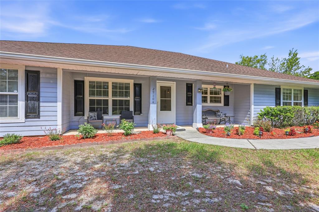 A light blue single-story house features a covered front porch and red mulch landscaping — 29104 N COUNTY ROAD 1491, ALACHUA, FL