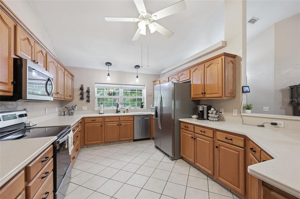 A kitchen with wood cabinets, stainless steel appliances, white countertops, and a tiled floor — 29104 N COUNTY ROAD 1491, ALACHUA, FL