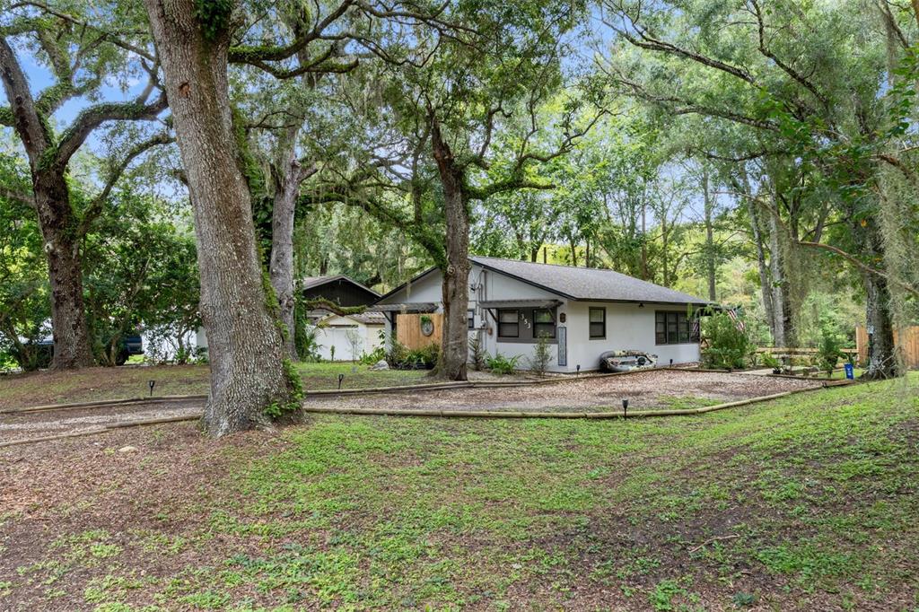 A single-story house with a gravel driveway sits among large, moss-draped oak trees — 353 N ROBIN HOOD ROAD, INVERNESS, FL