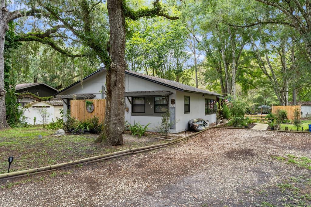 A single-story house with light gray siding sits on a gravel lot surrounded by trees — 353 N ROBIN HOOD ROAD, INVERNESS, FL