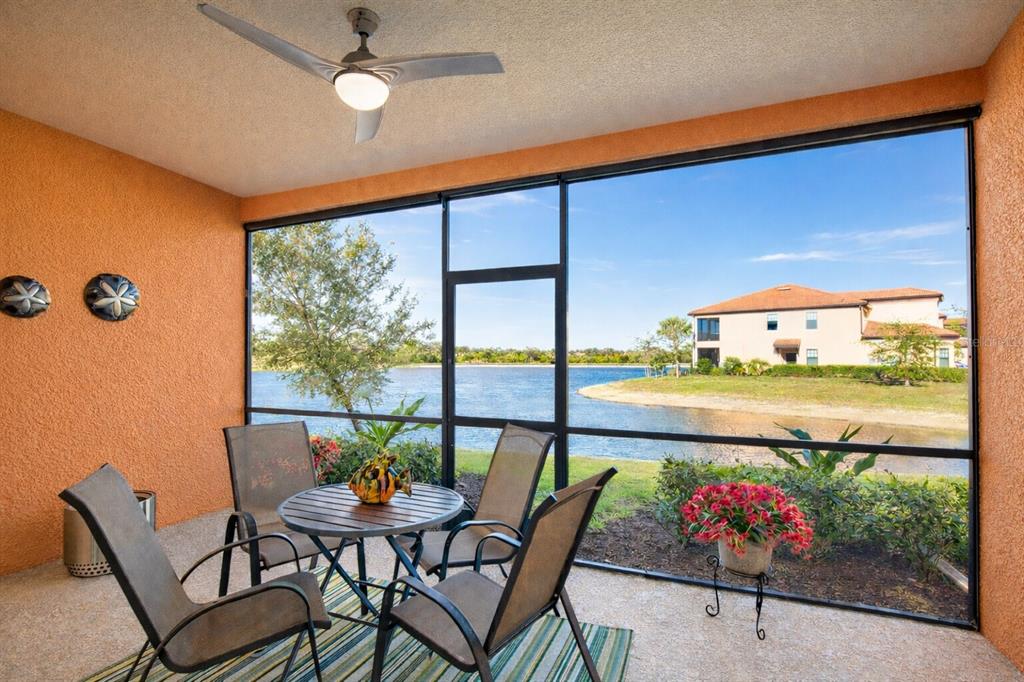 A screened-in patio with a dining set overlooks a lake and a neighboring building — 10042 CROOKED CREEK DRIVE UNIT 102, VENICE, FL