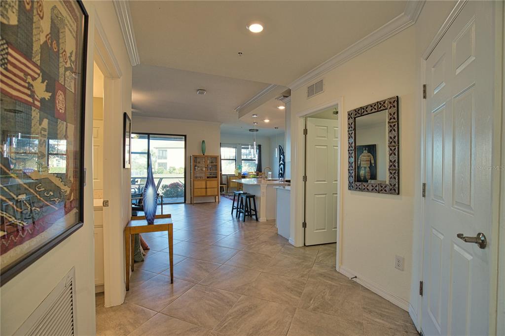 A tiled hallway leads to an open-concept kitchen and living area with sliding glass doors — 10042 CROOKED CREEK DRIVE UNIT 102, VENICE, FL
