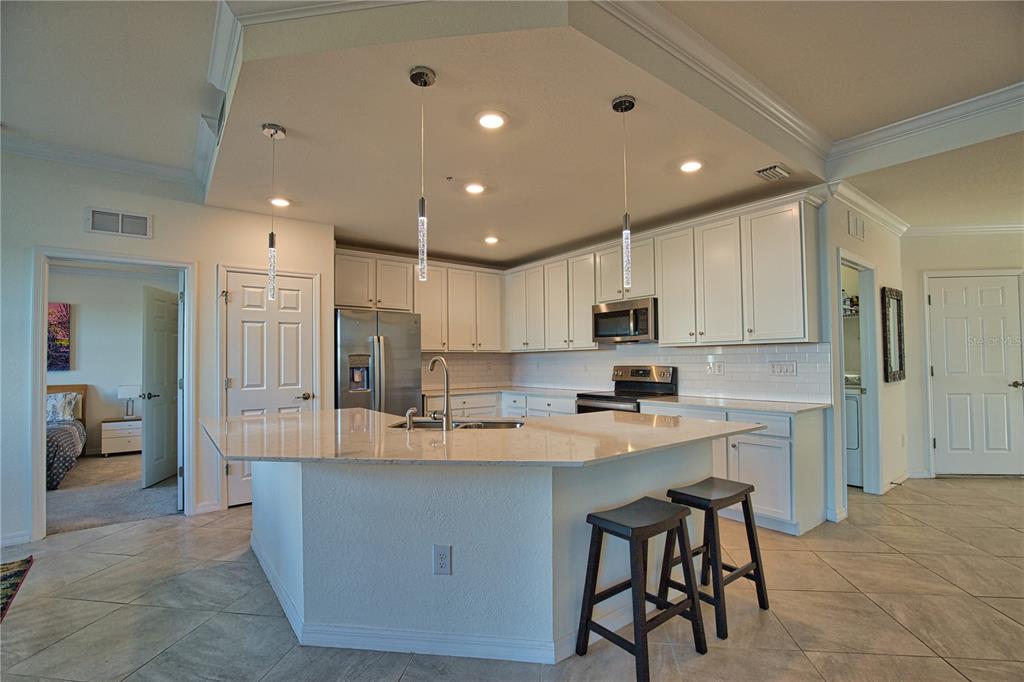 A kitchen with white cabinets, granite countertops, a central island, and two bar stools — 10042 CROOKED CREEK DRIVE UNIT 102, VENICE, FL