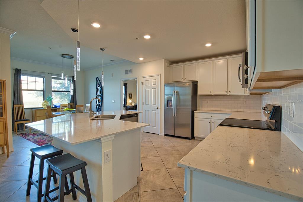 A kitchen features white cabinets, stainless steel appliances, a granite island, and tile flooring — 10042 CROOKED CREEK DRIVE UNIT 102, VENICE, FL
