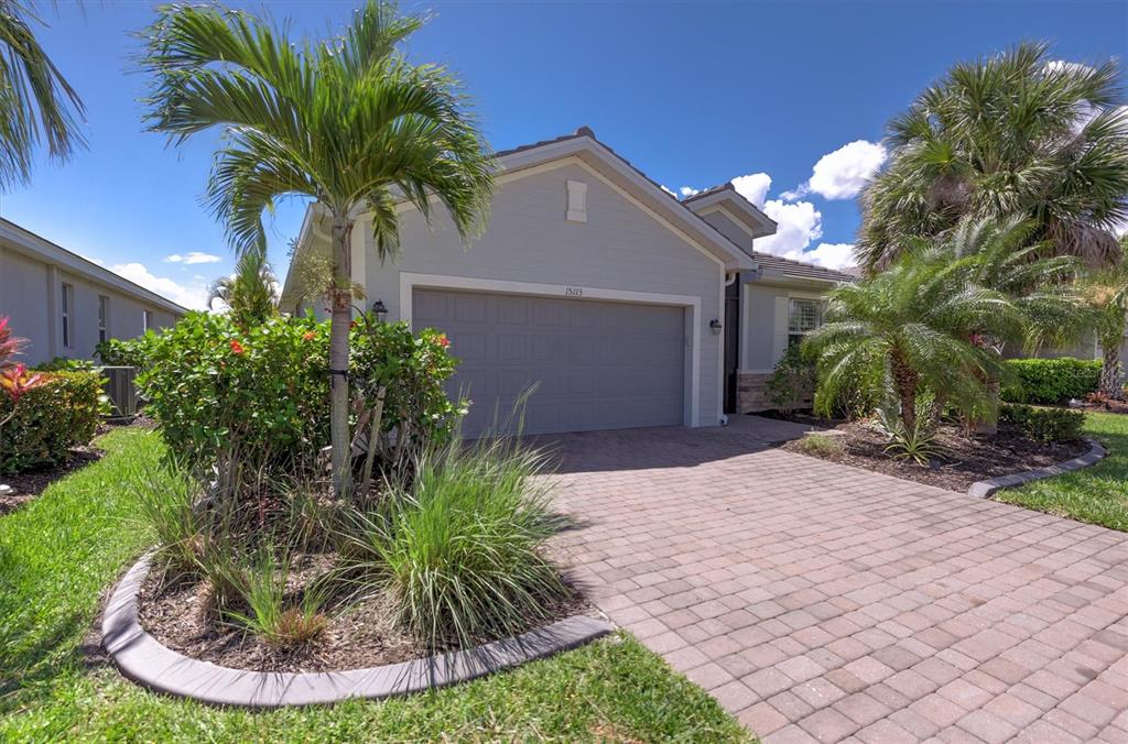 A single-story house with a gray garage, paver driveway, and palm trees under a blue sky — 15113 SPANISH POINT DRIVE, PORT CHARLOTTE, FL