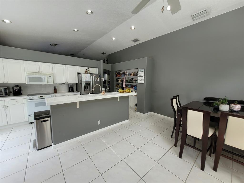 A kitchen with white cabinets, a gray island, and a dining table on tile floors — 6416 BARTON CREEK Circle, Lake Worth FL 33463, LAKE WORTH, FL