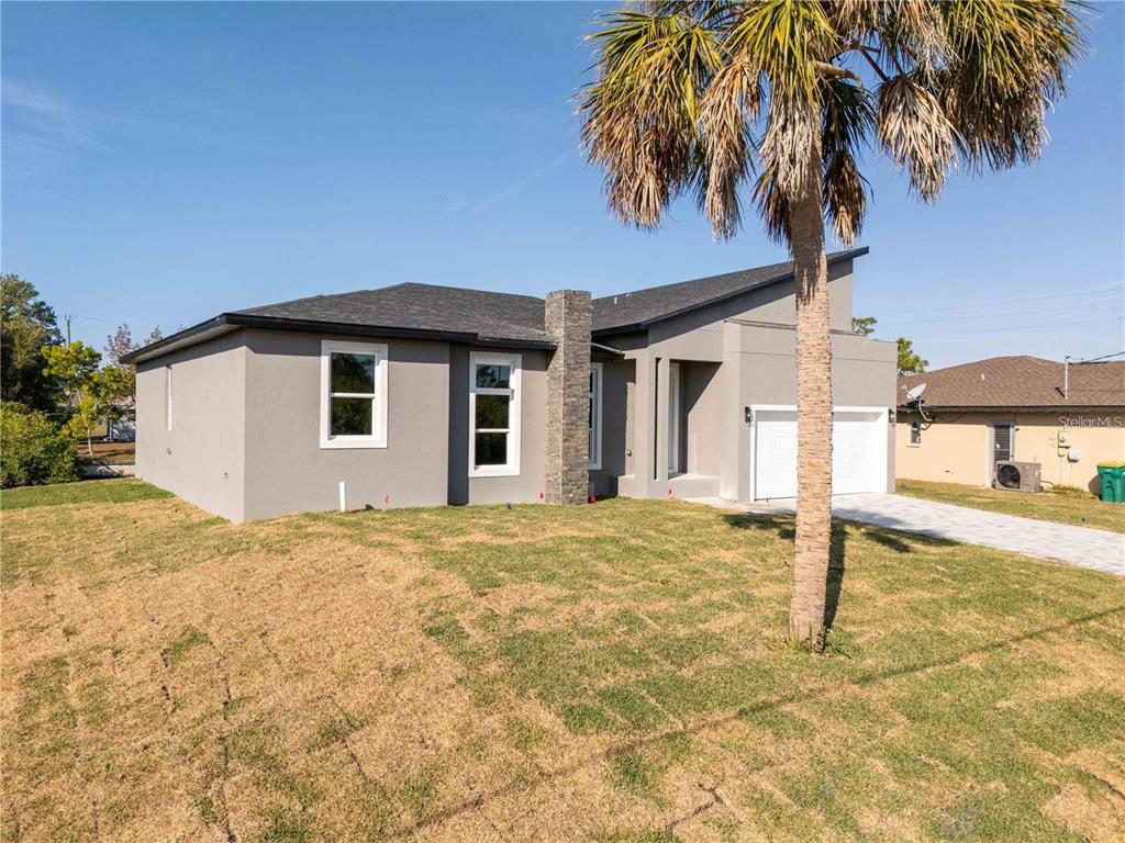 A modern, gray, single-story house with a stone chimney and a palm tree in front — 15 RAMBLEWOOD STREET, PORT CHARLOTTE, FL