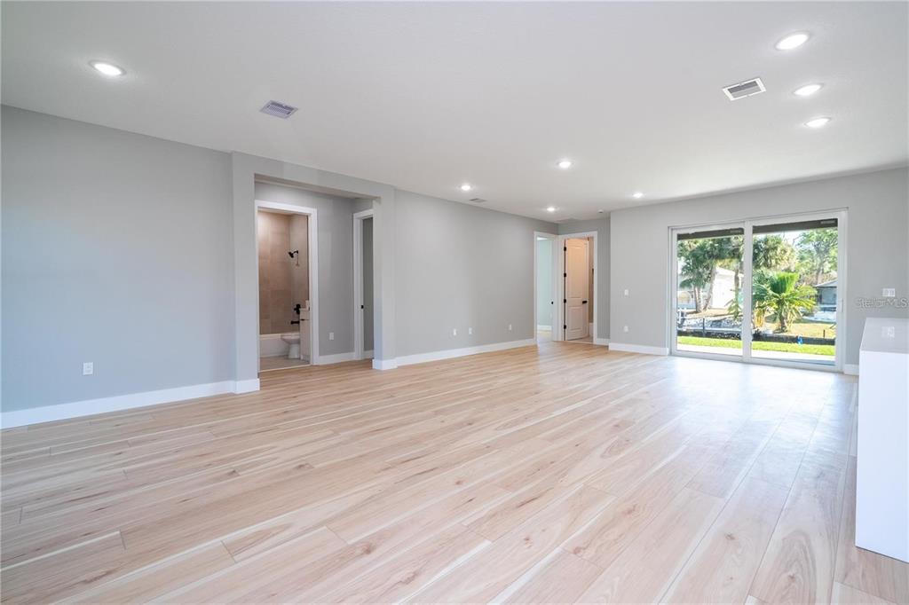 An empty room with light wood-look flooring, recessed lighting, and sliding glass doors to a yard — 15 RAMBLEWOOD STREET, PORT CHARLOTTE, FL