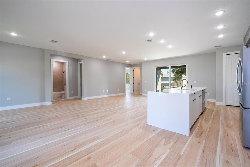 A bright, open-concept kitchen and living area featuring light wood flooring and a white island — 15 RAMBLEWOOD STREET, PORT CHARLOTTE, FL