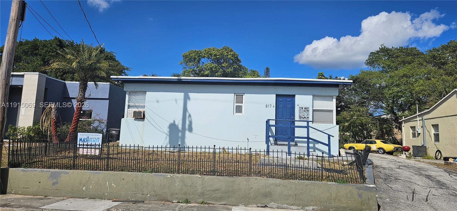 A light blue single-story house features a front porch, a blue door, and a fence — 817 Grant St, West Palm Beach FL 33407, WEST PALM BEACH, FL