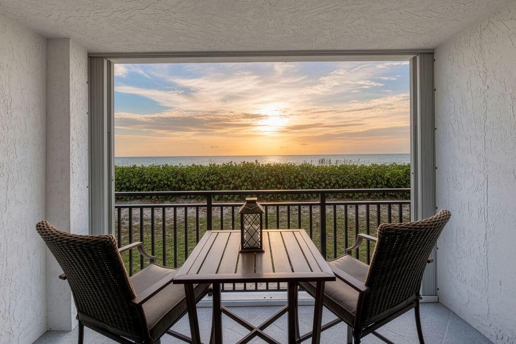 A covered balcony features two wicker chairs and a table overlooking the ocean at sunset — 10102 S Ocean Drive # 204a, Jensen Beach FL 34957, JENSEN BEACH, FL