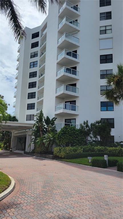 A multi-story white residential building features stacked balconies and a paved circular driveway entrance — 1000 LONGBOAT CLUB ROAD UNIT 406, LONGBOAT KEY, FL