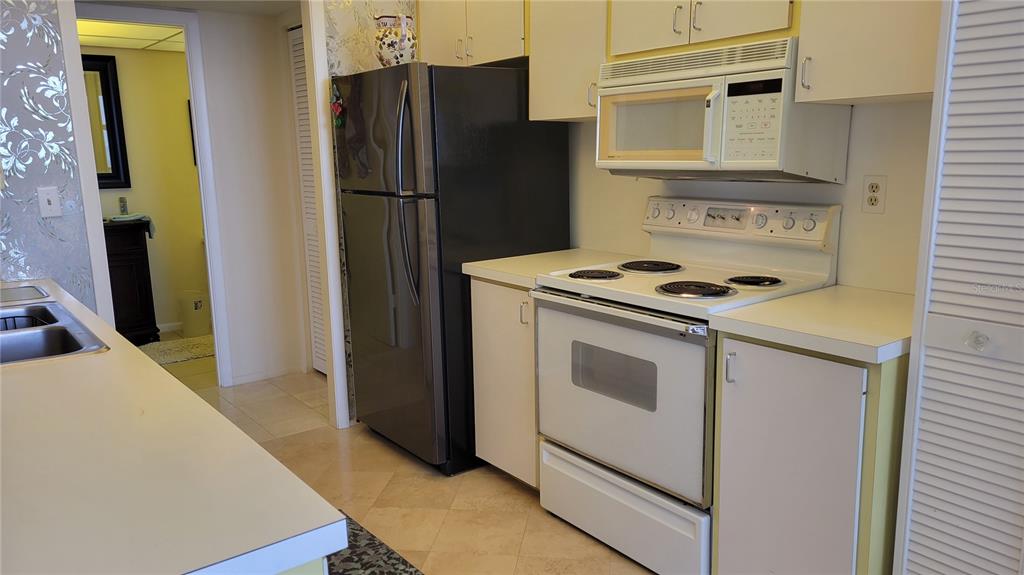 A kitchen features white cabinetry, a white electric stove, and a dark stainless steel refrigerator — 1000 LONGBOAT CLUB ROAD UNIT 406, LONGBOAT KEY, FL