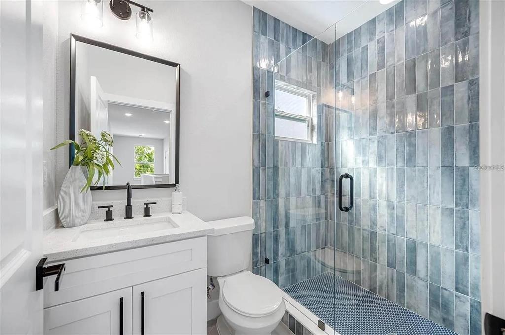 A bathroom features a white vanity, a toilet, and a glass-enclosed shower with blue tiles — 1516 59TH STREET N, ST PETERSBURG, FL
