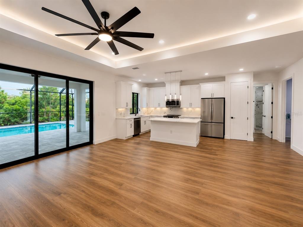 A modern kitchen with white cabinetry and an island opens to a pool patio area — 32 SALUDA TERRACE, PORT CHARLOTTE, FL