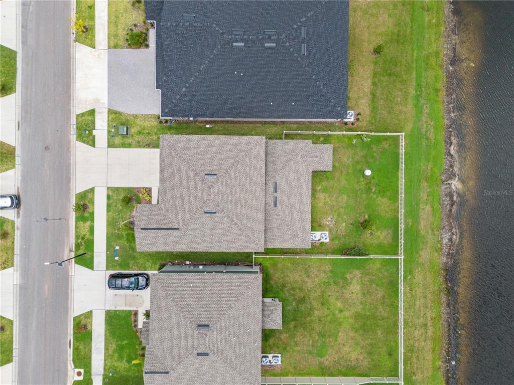 An aerial view shows three suburban houses with fenced backyards bordering a body of water — 22313 PLEASANT MORNING DRIVE, LAND O LAKES, FL