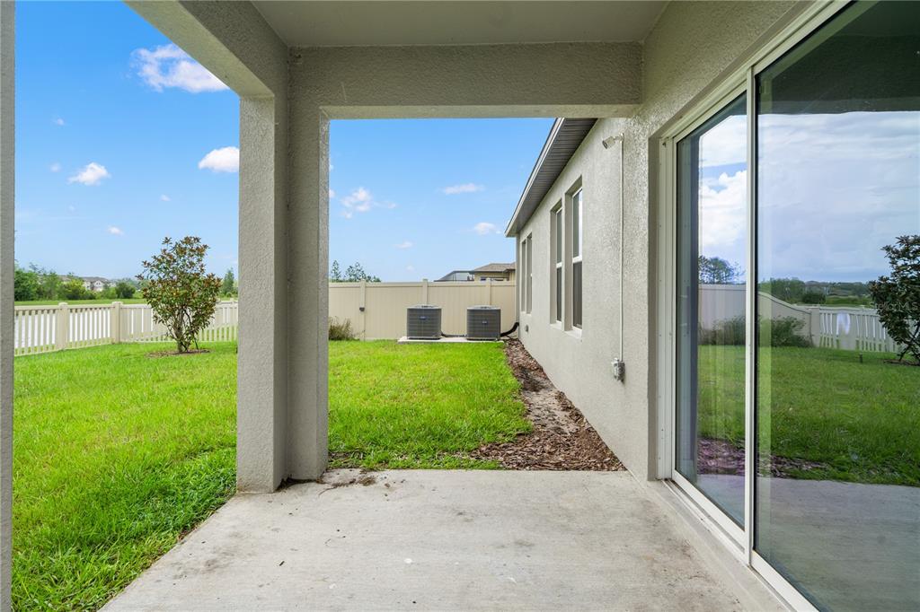 A covered concrete patio overlooks a grassy backyard with two air conditioning units and fencing — 22313 PLEASANT MORNING DRIVE, LAND O LAKES, FL