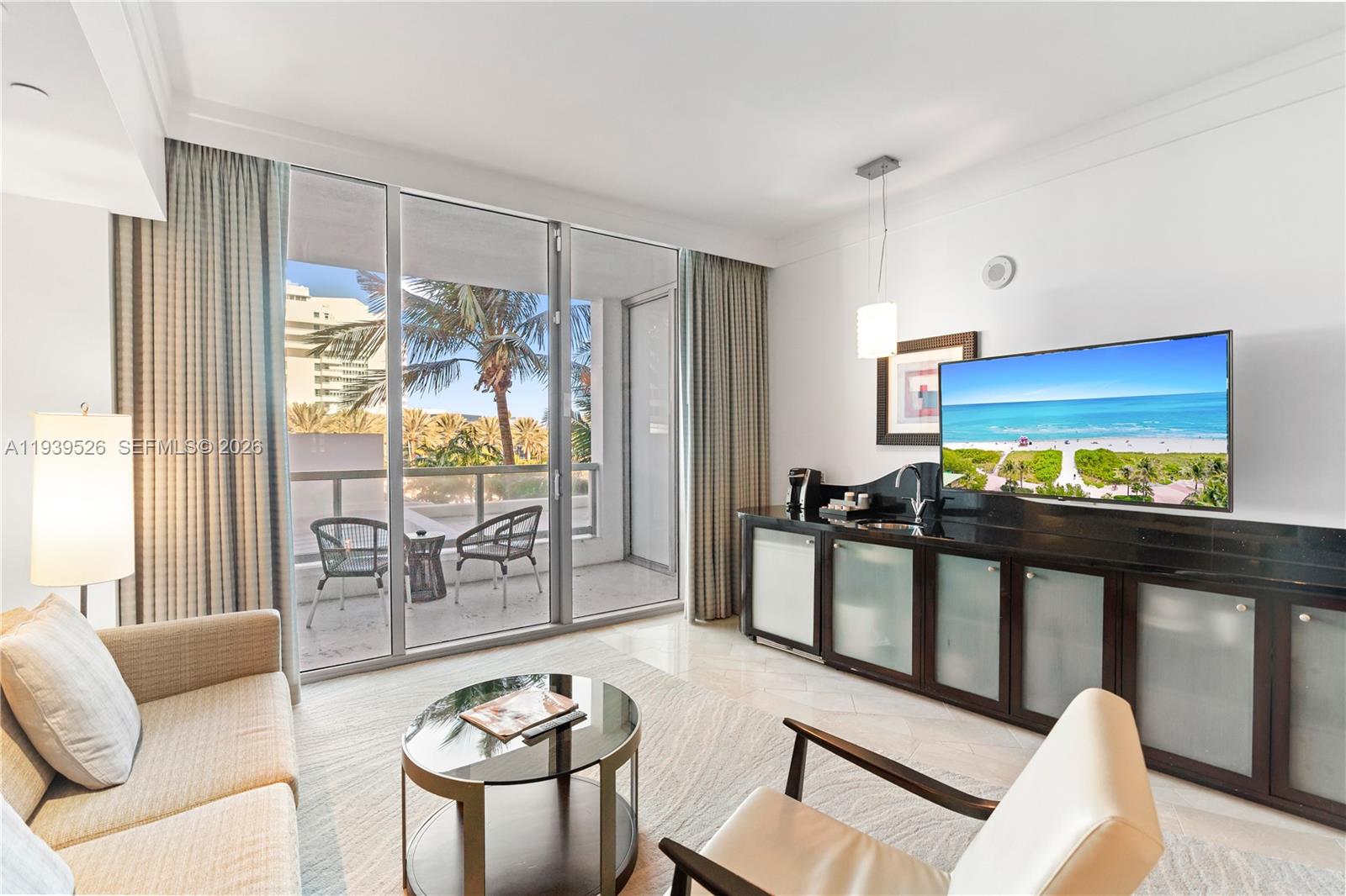 A living room features a sofa, armchairs, a television, and a balcony with palm trees — 4391 Collins Ave # 303, Miami Beach FL 33140, MIAMI BEACH, FL