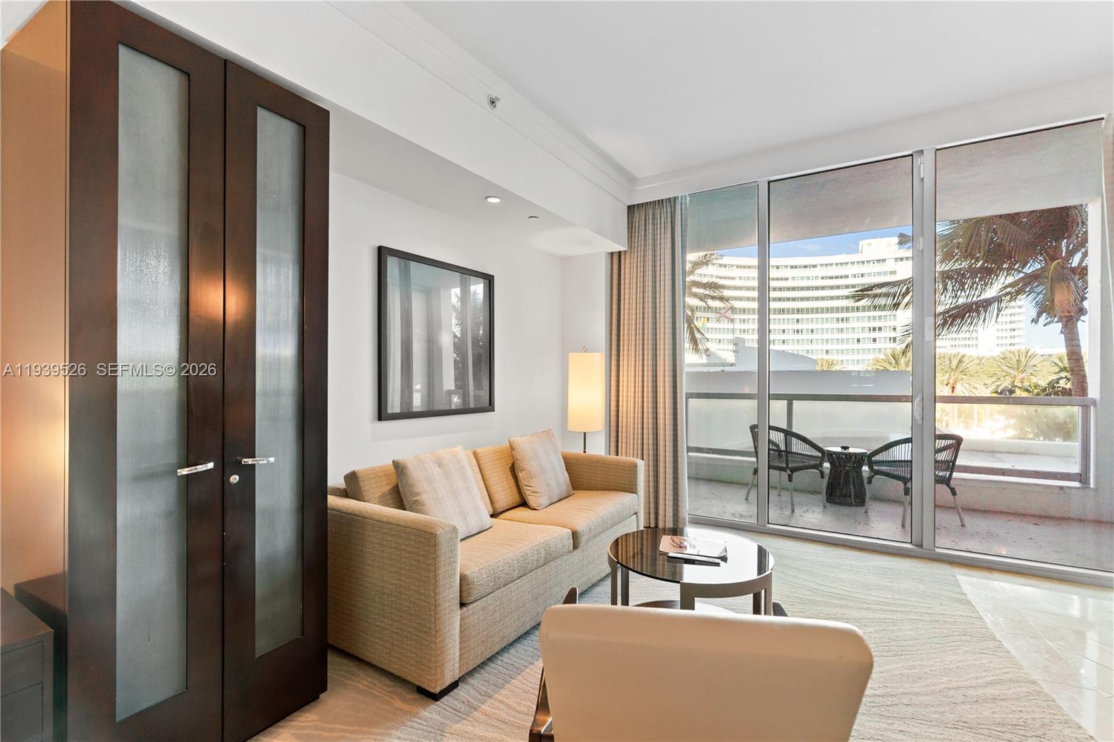 A living room features a beige sofa, a glass coffee table, and a balcony view — 4391 Collins Ave # 303, Miami Beach FL 33140, MIAMI BEACH, FL