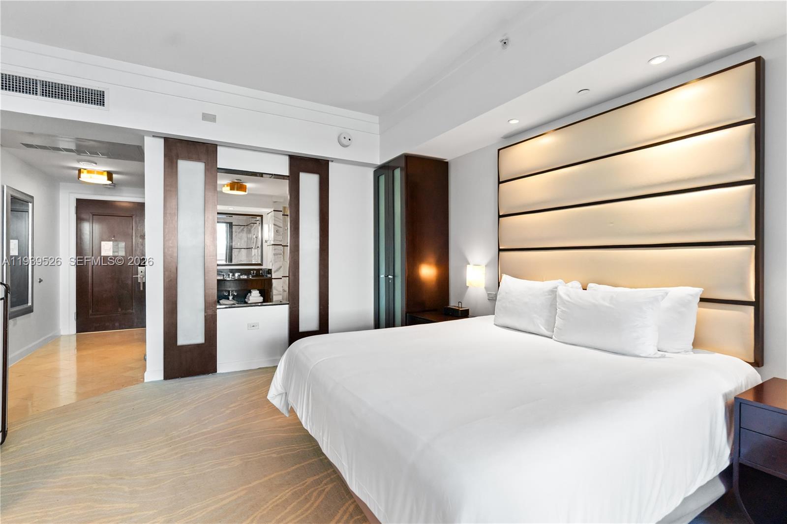 A bedroom features a large bed with a tall, horizontal-paneled headboard and an attached bathroom — 4391 Collins Ave # 303, Miami Beach FL 33140, MIAMI BEACH, FL