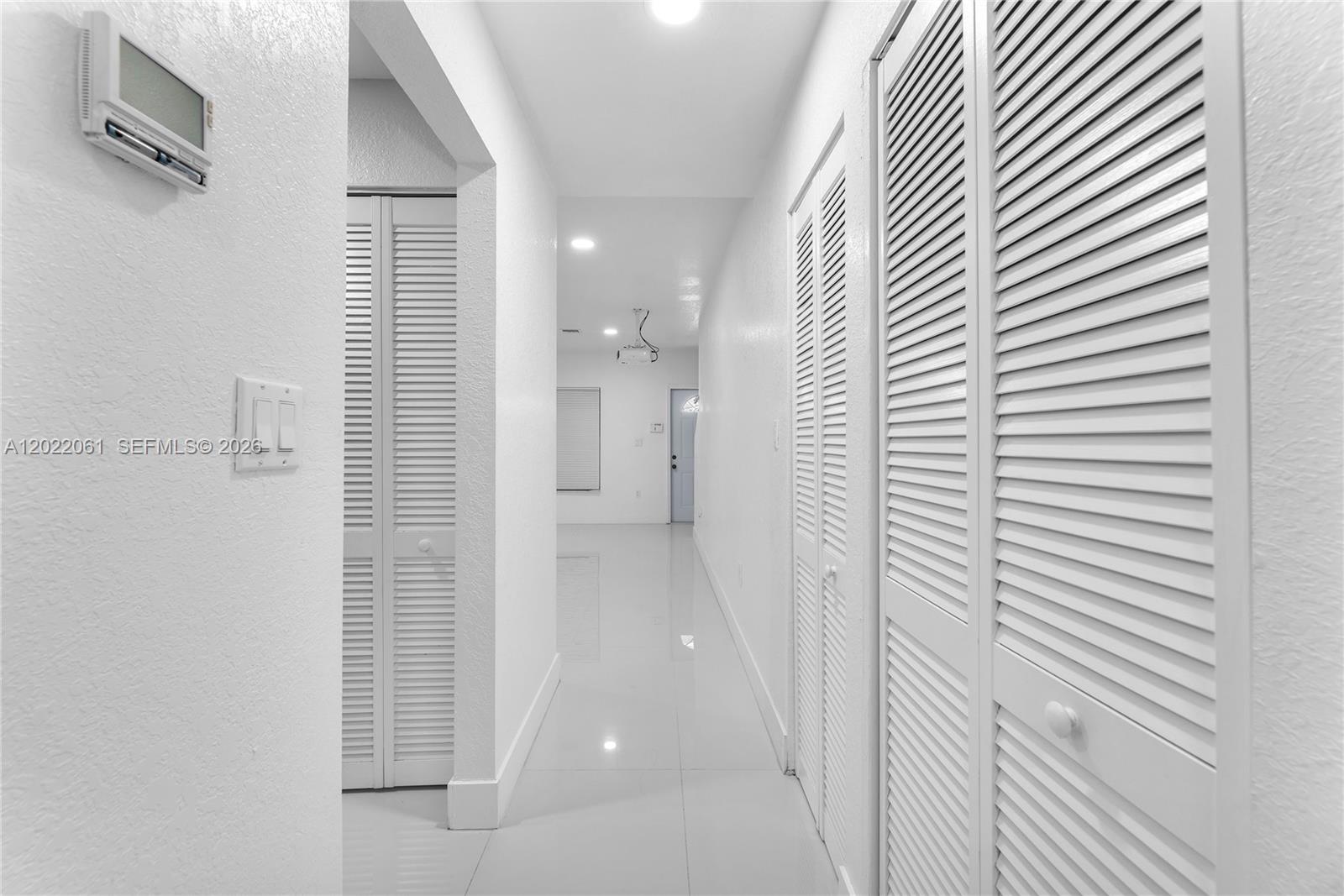 A white hallway features tiled floors, louvered closet doors, and a wall-mounted thermostat — 1541 NW 1st Ct, Miami FL 33136, MIAMI, FL