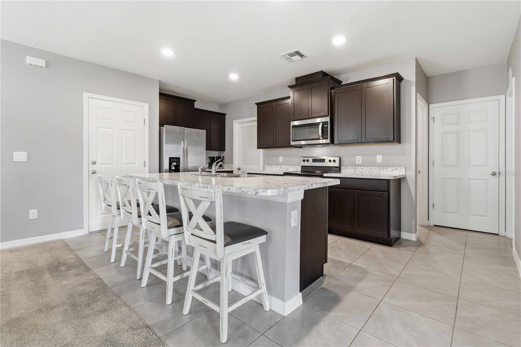 A kitchen features dark wood cabinets, a marble-patterned island with bar stools, and tile flooring — 1156 VALLEY VIEW AVENUE, ROCKLEDGE, FL