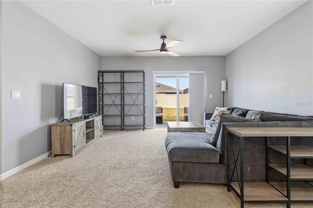 A living room with gray walls, carpeted flooring, a sectional sofa, and a sliding glass door — 1156 VALLEY VIEW AVENUE, ROCKLEDGE, FL