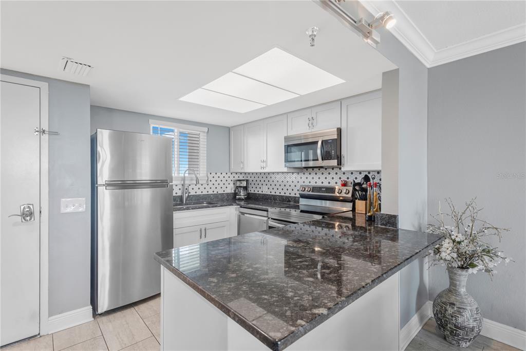 A kitchen features stainless steel appliances, white cabinets, dark granite countertops, and a tiled backsplash — 5915 SEA RANCH DRIVE UNIT 503, HUDSON, FL
