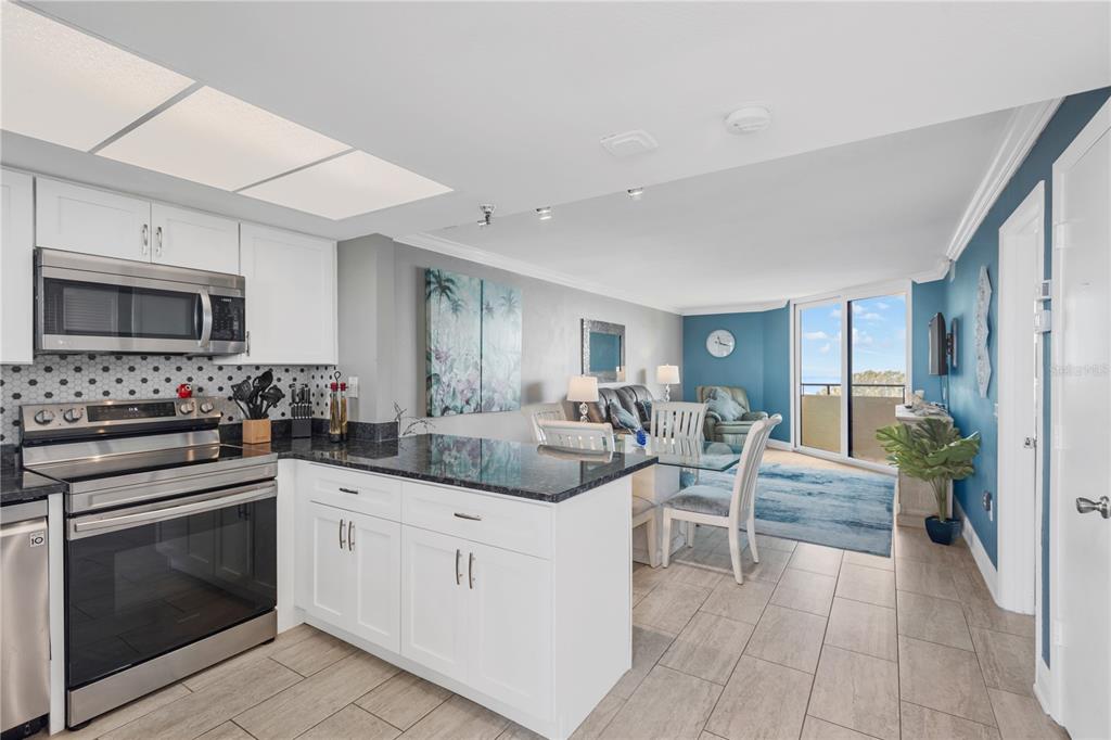 A kitchen with white cabinets and granite countertops opens into a dining and living area — 5915 SEA RANCH DRIVE UNIT 503, HUDSON, FL