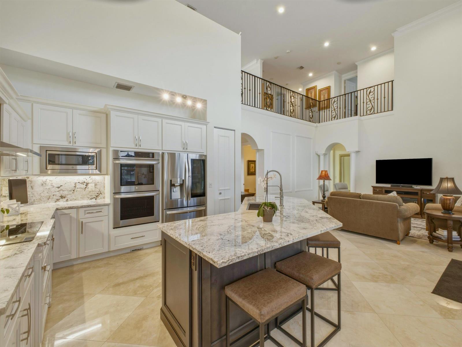 A kitchen with white cabinets and a dark island overlooks a living room with balcony — 9814 Coronado Lake Drive, Boynton Beach FL 33437, BOYNTON BEACH, FL