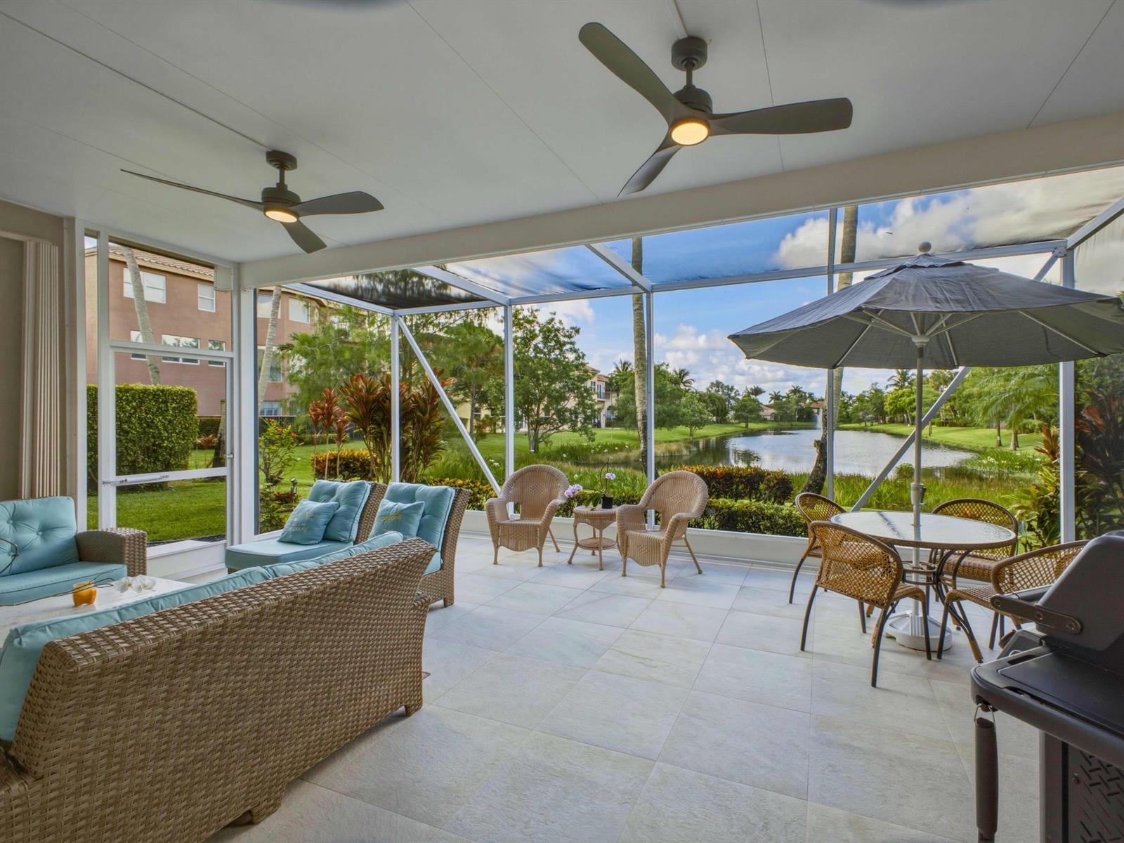 A screened-in patio features tile flooring, wicker furniture, ceiling fans, and a view of water — 9814 Coronado Lake Drive, Boynton Beach FL 33437, BOYNTON BEACH, FL