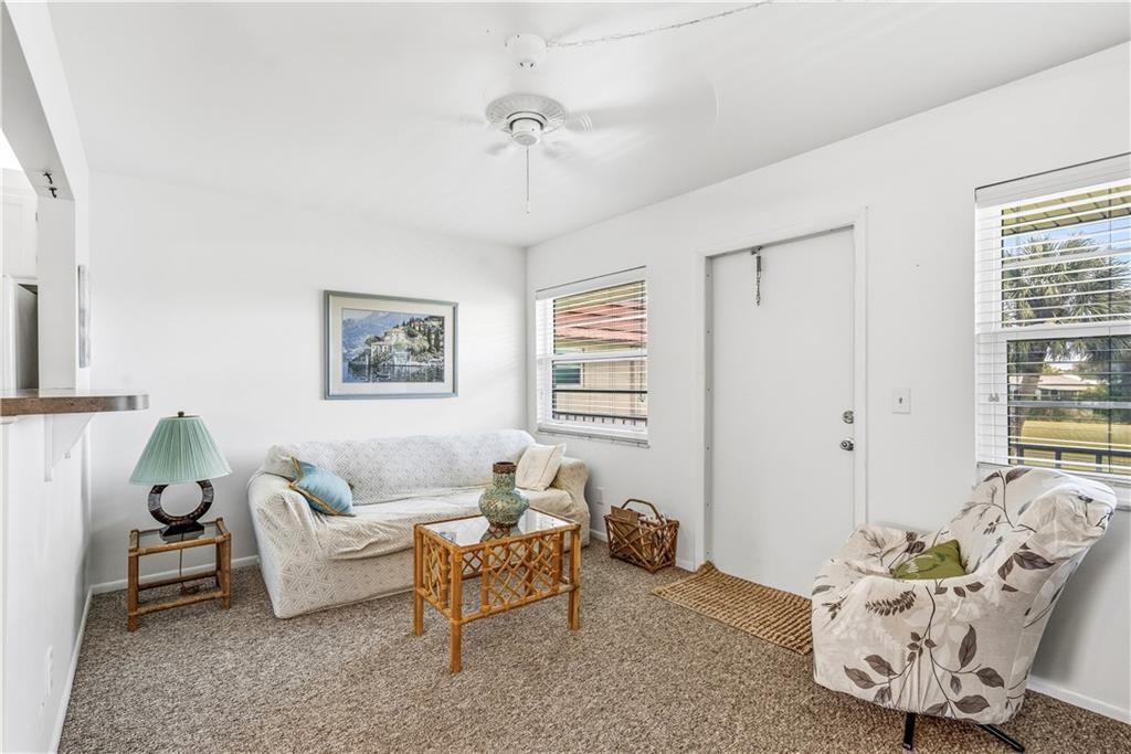 A living room features a sofa, patterned armchair, glass-topped coffee table, and a ceiling fan — VERO BEACH, FL
