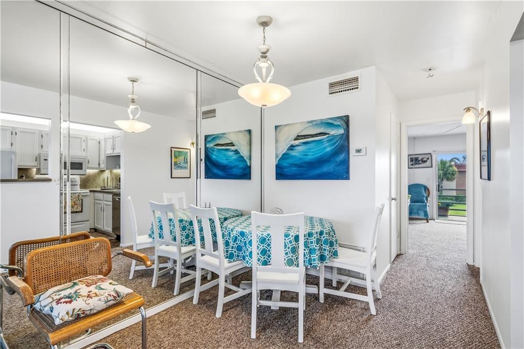 A dining area with a round table, white chairs, mirrored walls, and carpeted flooring — VERO BEACH, FL