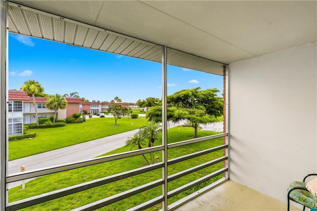 A screened-in balcony overlooks a grassy courtyard with palm trees and a paved driveway — VERO BEACH, FL