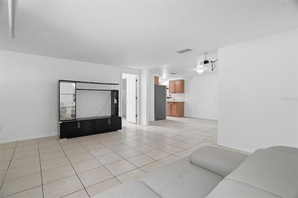A living room with light tile floors, a black media console, and an adjacent kitchen — 8855 53RD WAY N, PINELLAS PARK, FL